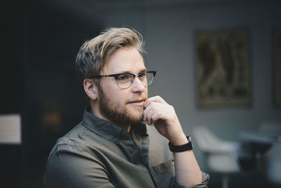 Thoughtful male computer programmer with hand on chin looking away in office