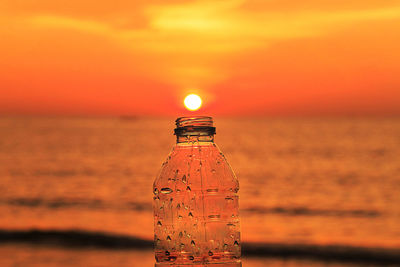 Close-up of bottle against sea during sunset