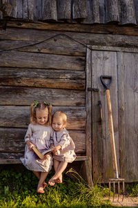 
low angle view of two children reading a book sitting on a wooden bench near an old bathhouse