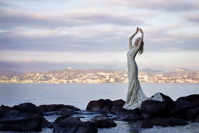 Full length of woman standing on rock in sea against sky