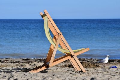 Deck chair on sand against sea