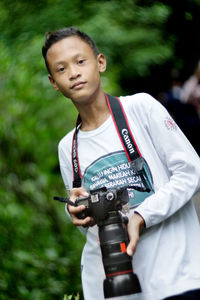 Full length of man holding camera while standing outdoors