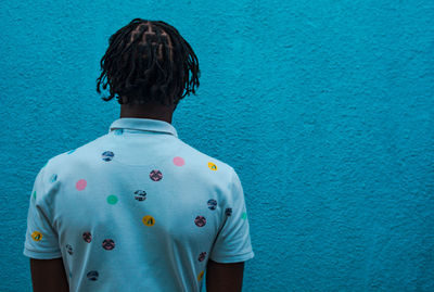 Rear view of a young adult standing against blue wall