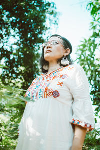 Portrait of young woman standing against trees