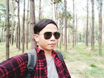 Man wearing sunglasses while standing against trees in forest