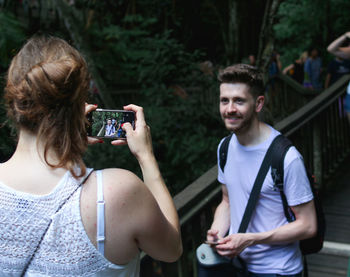 Rear view of woman photographing smiling man in forest