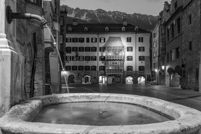 Fountain in city street amidst buildings at night