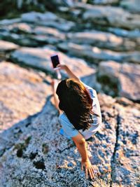 Rear view of woman using phone on rock