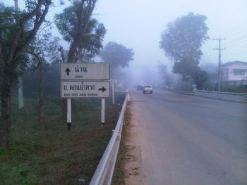 Road sign by trees against sky