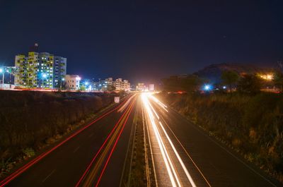 Light trails on road in city against sky at night