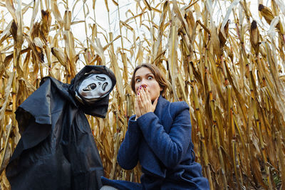 Woman with frightened face near figure with death mask in cornfield on halloween