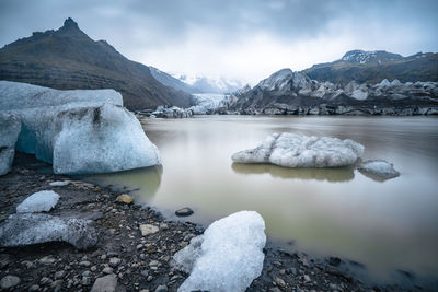 Ice floating in muddy waters of glacier lake with glacier in background on a cloudy and rainy day.