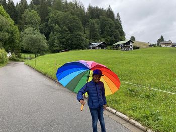 Boy  standing by multi colored umbrella on road during rainy season