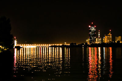 Illuminated city by river against clear sky at night