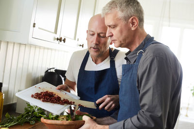 Bald mature man assisting friend in cooking food at home