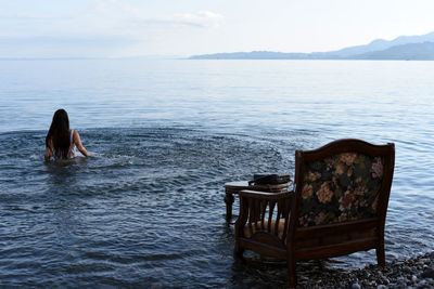 Rear view of woman sitting by sea against sky