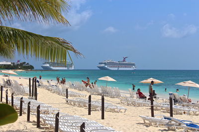 People and deck chairs at beach against sky