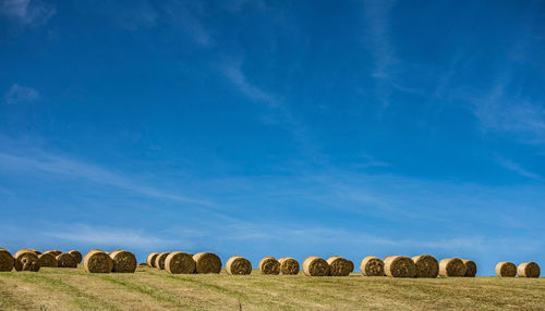 Hay bales on field against blue sky