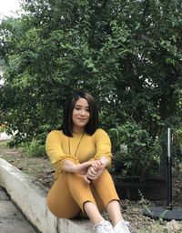 Portrait of young woman sitting against trees in park