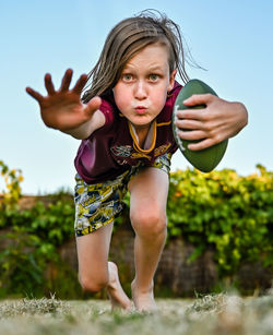 Portrait of boy making face jumping while standing outdoors