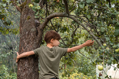 Side view of boy standing against tree