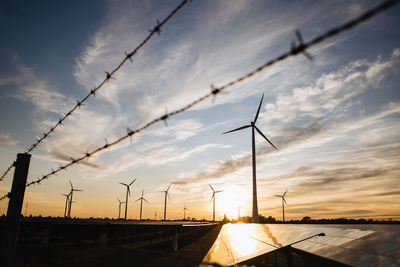 Low angle view of wind turbines against sky during sunset