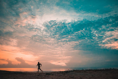 Silhouette man running on beach against sky during sunset
