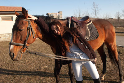 Portrait of young woman standing with horse against sky