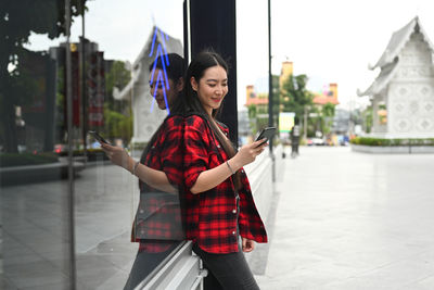 Young woman using phone while standing on city