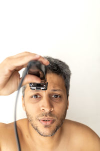 Portrait of young man holding camera against white background