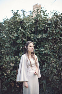 Thoughtful fairy elf young woman standing by plants