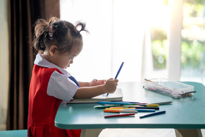 Side view of girl drawing in book at table