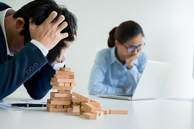 Stressed businessman with block removal game while businesswoman using laptop in office