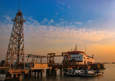 Cranes at commercial dock against sky during sunset