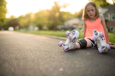 Girl wearing roller skates sitting on road at park