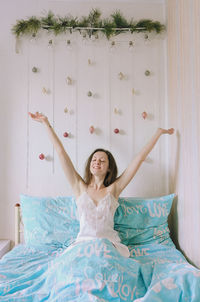 Cheerful woman sitting on bed with arms raised