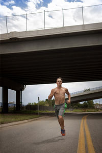 Male athlete running on road under bridge