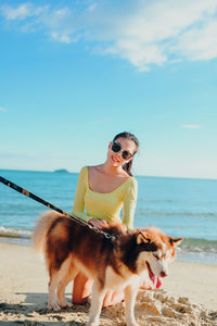 Portrait of woman with dog on beach against sky