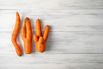 Top view close-up of several ripe orange ugly carrots lie on a light wooden surface 