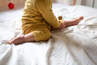 Close-up view on legs of sitting on the bed baby in yellow pyjamas