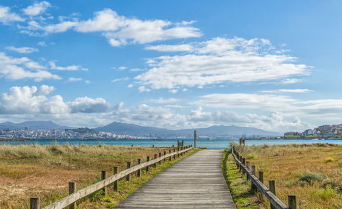 Boardwalk leading towards sea against sky