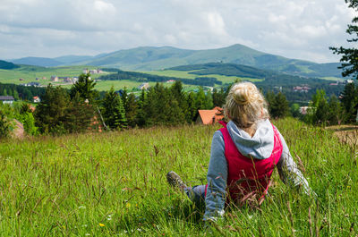 Blond woman sitting on mountain meadow and enjoying a mountain landscape in springtime