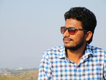 Young man wearing sunglasses standing against clear sky