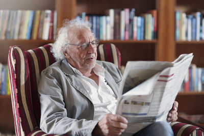 Senior man sitting in library, reading newpaper