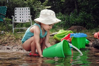 Girl filling water in bucket while crouching on lakeshore