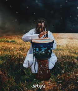 Woman holding umbrella while sitting on field