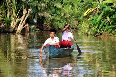 Full length of couple sitting on lake against trees