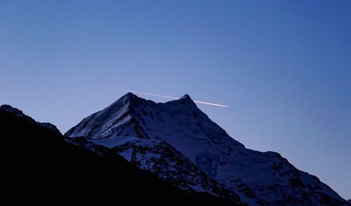 Low angle view of snowcapped mountains against clear blue sky