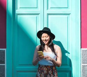 Young woman holding smart phone while standing against door