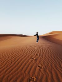 Full length of man on sand dune in desert against clear sky